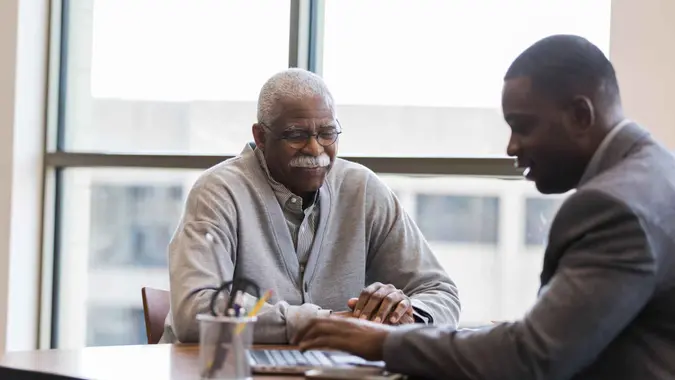 The mid adult loan officer patiently and cheerfully help sthe senior man find the best investment option for retirement savings.