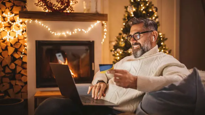 Mature man sitting on couch at cottage for Christmas and using laptop.