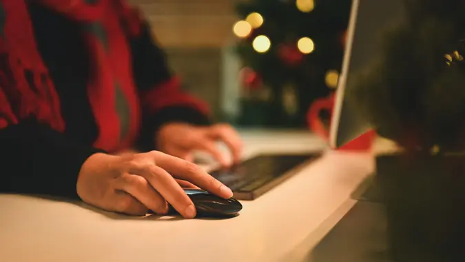 Closeup woman hands using wireless mouse while working on computer at table against Christmas tree stock photo