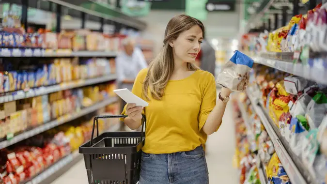Female consumer purchasing goods at grocery store, walking among shelves.
