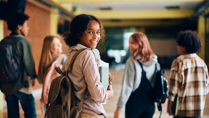 Happy African American high school student walking through hallway with her friends and looking at camera.