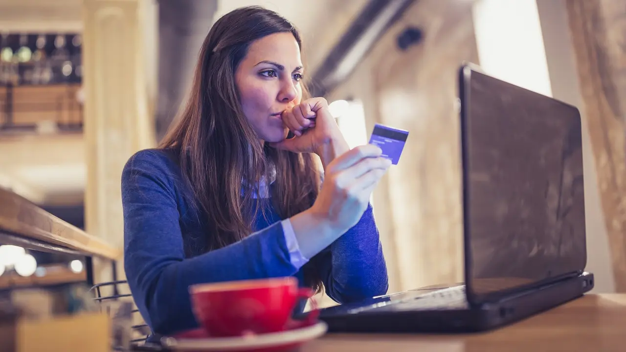 A young woman in a cozy cafe, deeply engrossed in online shopping on her laptop, pays seamlessly with a credit card.
