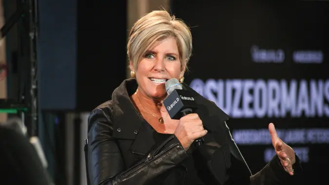 Suze Orman holds a microphone while speaking during an event.