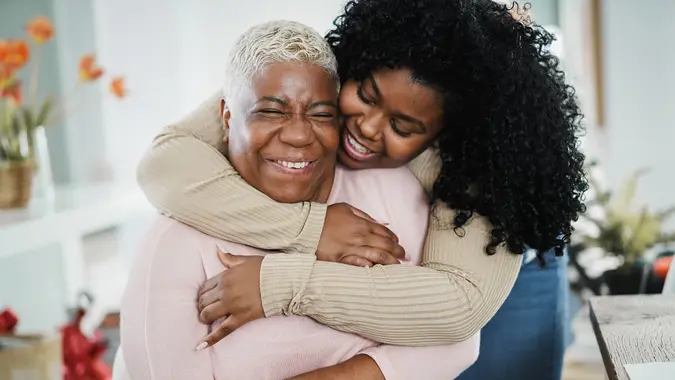 African daughter hugging her mum indoors at home - Main focus on senior woman face stock photo