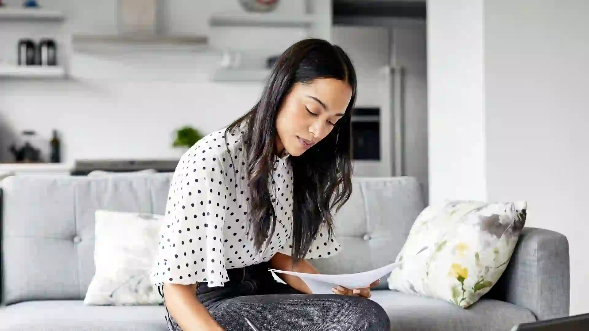 A woman sits on the couch while she analyzes her budget.