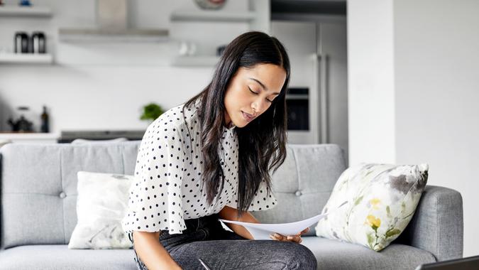 A woman sits on the couch while she analyzes her budget.