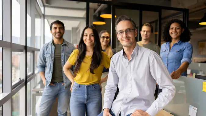 A group of happy co-workers smile and look into the camera while meeting at work.
