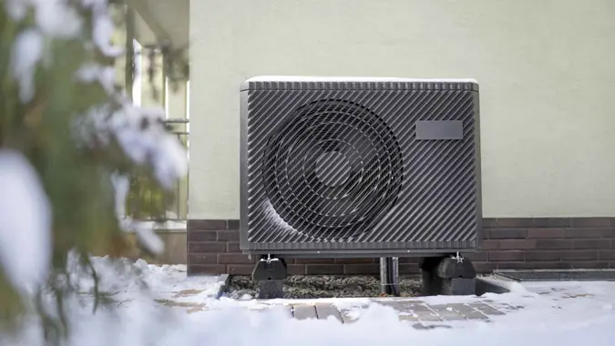 Photo of a modern air source heat pump unit standing against the residential building wall.