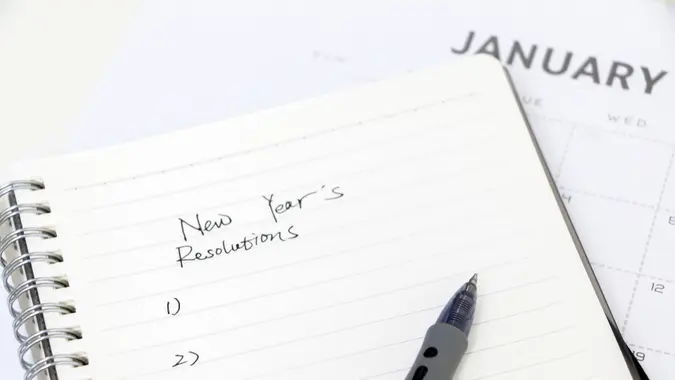 Writing new years resolutions, list on notepad with ballpoint pen, January calendar in background, selective focus.