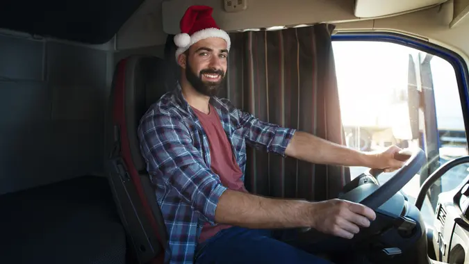 Truck driver wearing Santa Clause hat and driving his truck on Christmas. People working on holidays. Trucker lifestyle. Merry Christmas. stock photo