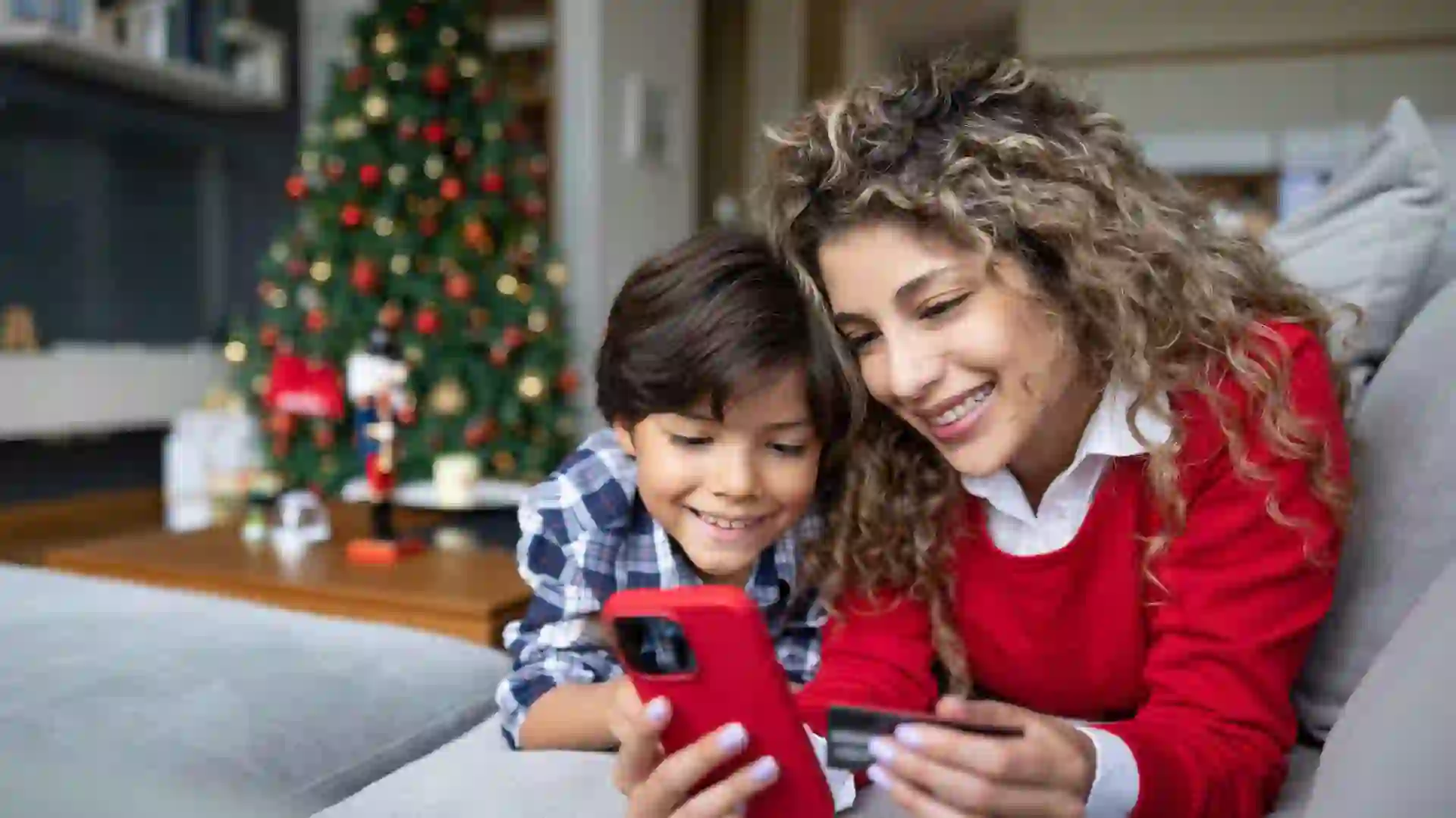Happy mother and son shopping their Christmas presents online using her cell phone and paying by credit card - e-commerce concepts.