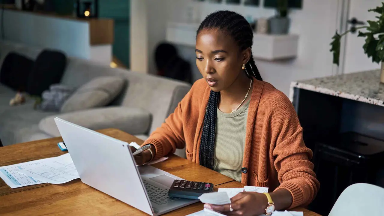 A woman sits in front of her laptop and does calculations.