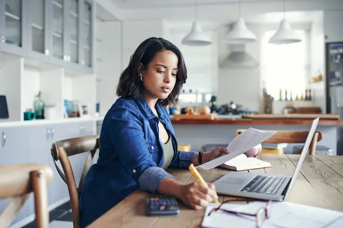 A woman works at her desk in her kitchen at home.
