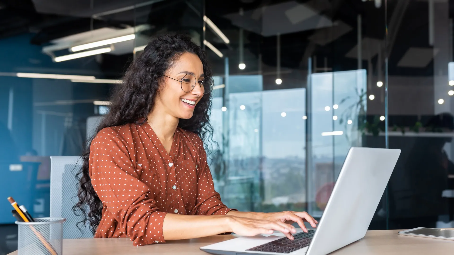 A woman smiles as she types on her laptop at work.