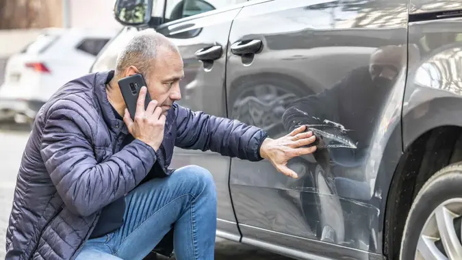 A man calls the insurance company or the police because someone backed into the side door of his car in the parking lot.