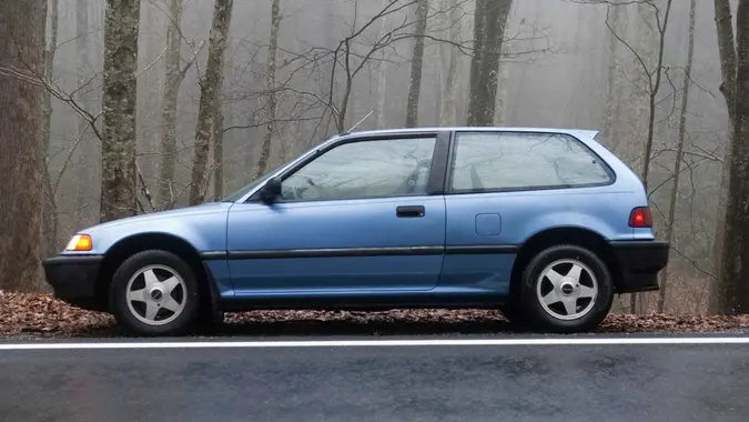 Shady Valley, TN, USA - November 30, 2009: A blue 1991 Honda Civic hatchback parked on the edge of a wet road in a foggy forest.