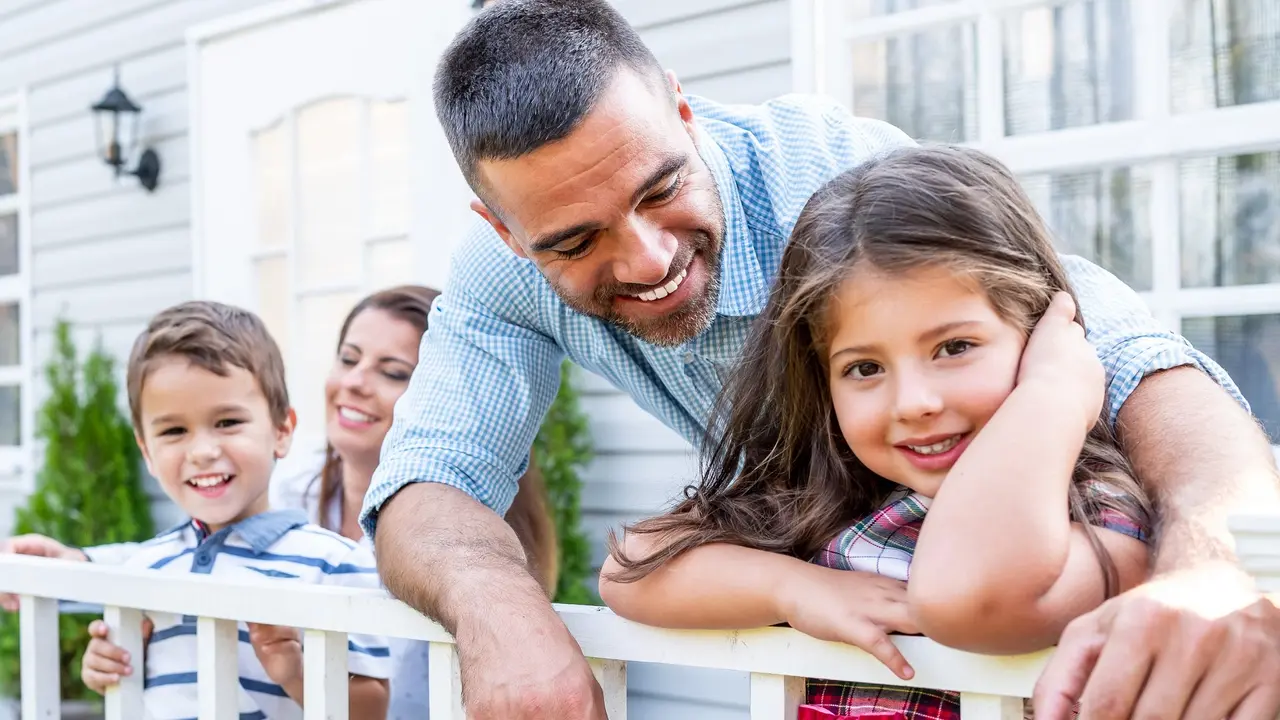 Happy family with two kids sitting in front of american porch, smiling together.