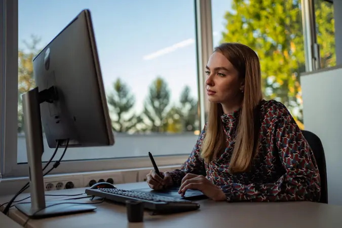 Female graphic designer is sitting in the office and drawing on the graphic board.