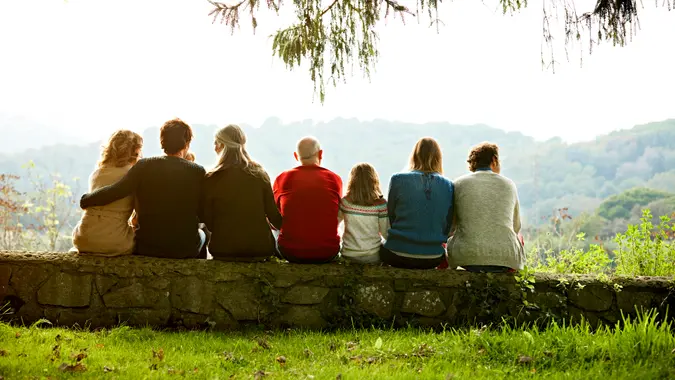 Rear view of multi-generation family relaxing in row on retaining wall against clear sky.