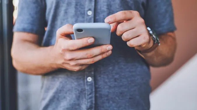 Closeup of man hands on a phone browsing on social media while standing outdoors in the city street. Guy reading an article or blog on a website with a smartphone in an urban town road. stock photo