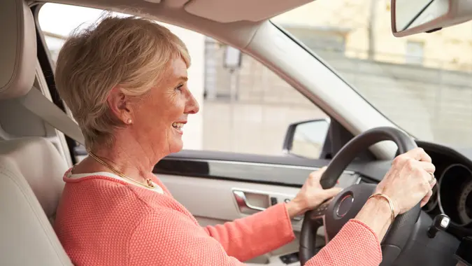 A retired woman smiles as she drives her car.