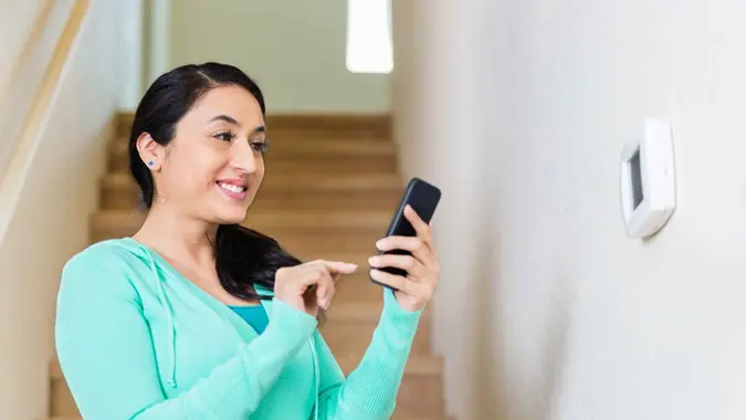 Pretty mid adult Hispanic woman uses smart phone to control temperature of home.