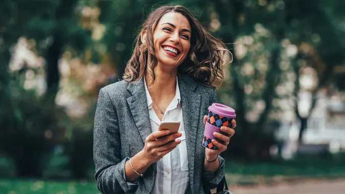 Shot of a Young woman texting on a phone and drinking a coffee while walking in the park stock photo