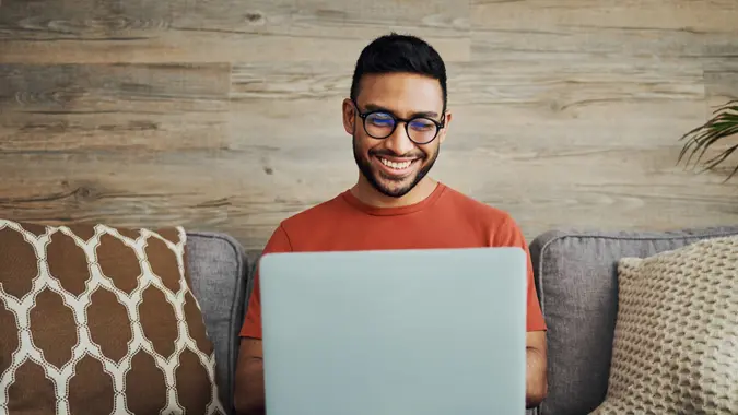 A man smiles and looks happy while looking at his laptop at work.