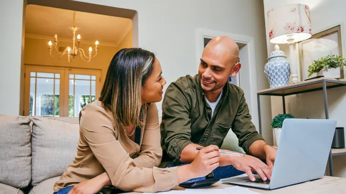 A couple manages their finances will working on their laptop and sitting in the living room.