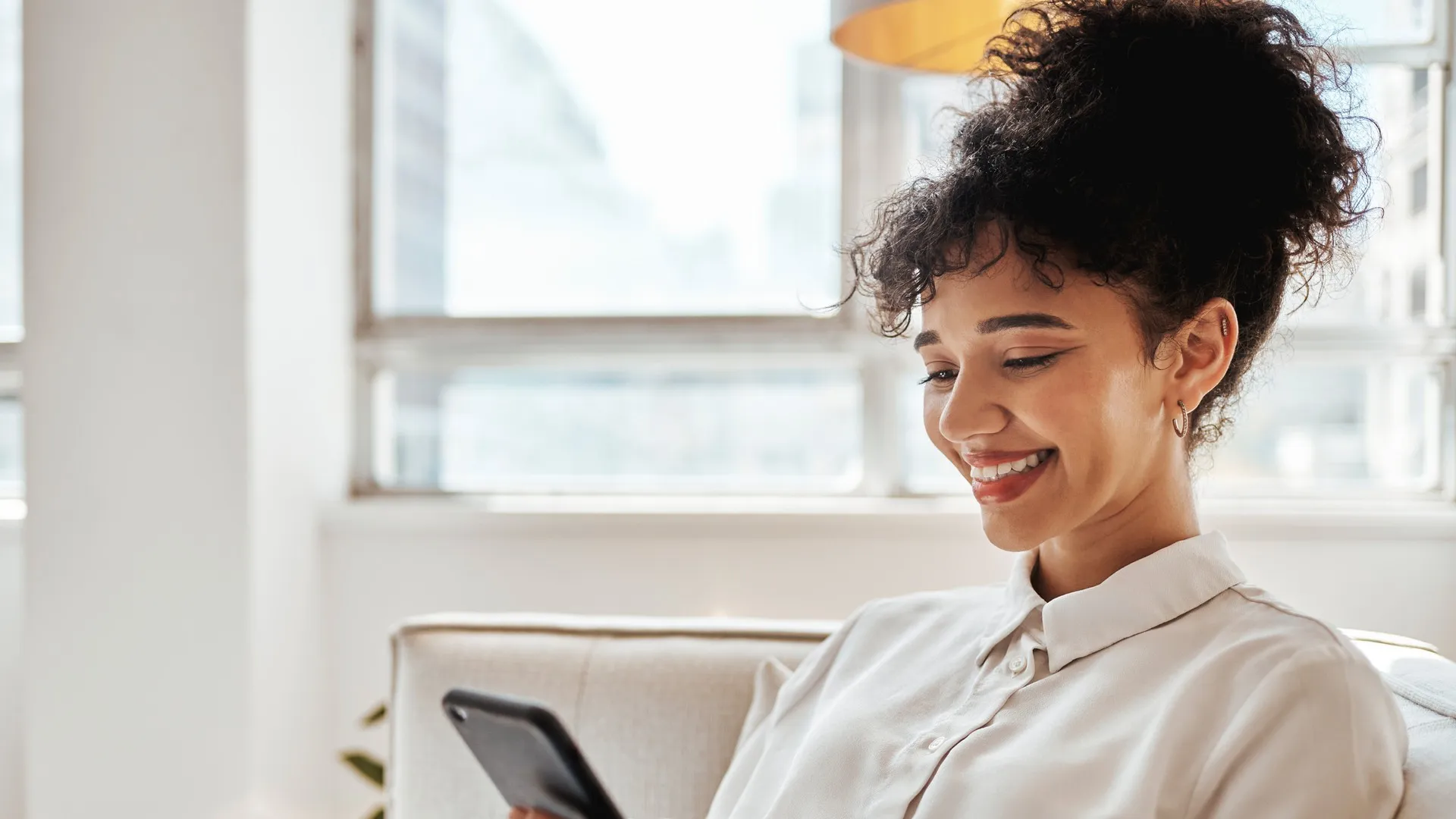 A woman smiles as she looks at her phone while working from home.