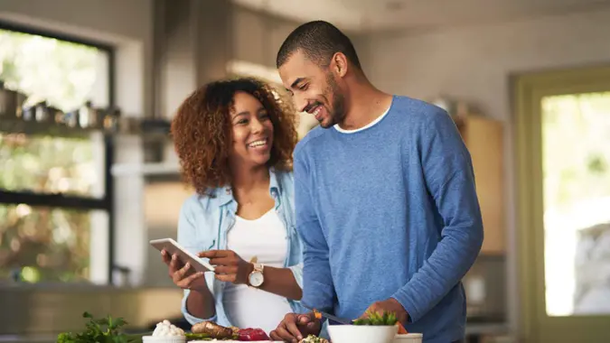Shot of a happy young couple using a digital tablet while preparing a healthy meal together at home.