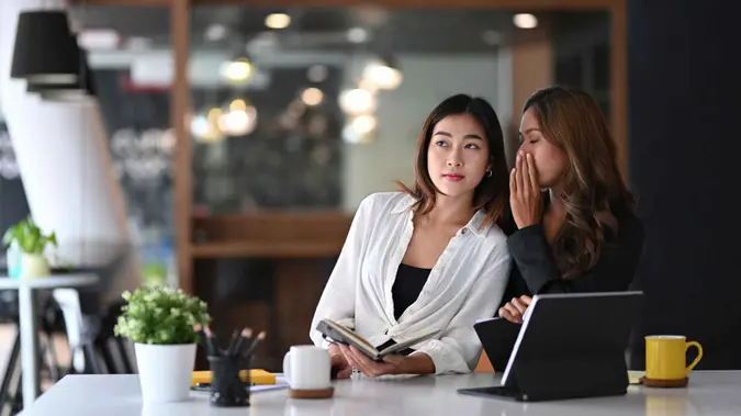 Business woman whispering something  in ear of her colleague.