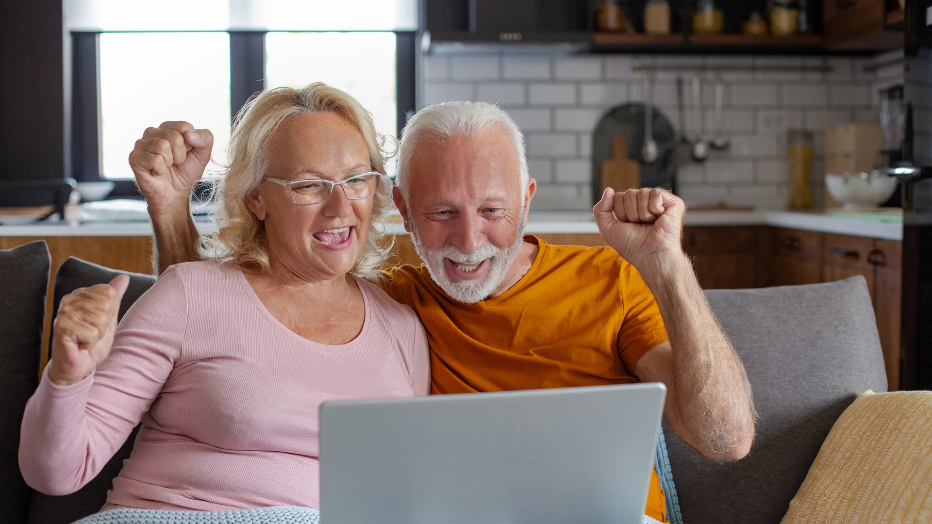 A happy retired couple looks at their laptop and raise their hands.