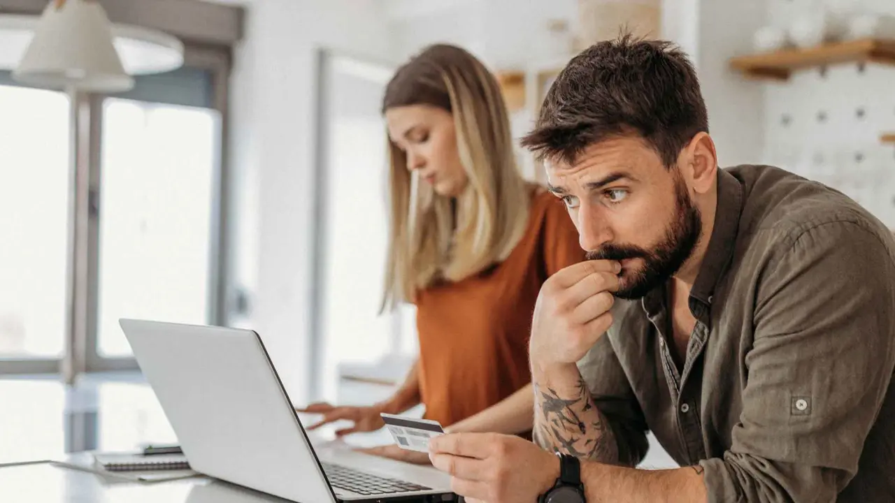 A couple in their kitchen holding a credit card while reviewing finances and planning their monthly budget together.