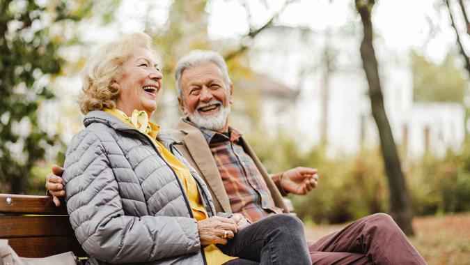 A happy senior couple sitting on a bench together in warm clothing.