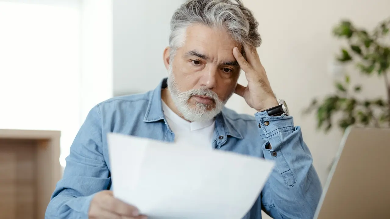 A man looks stressed and worried as he looks at tax or financial paperwork.