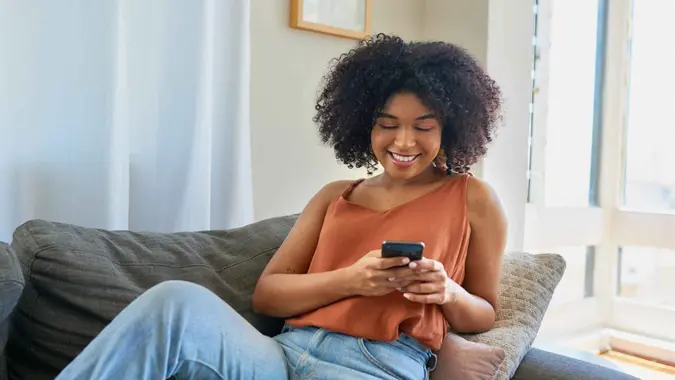 Shot of a young woman using a cellphone while relaxing on a sofa at home.