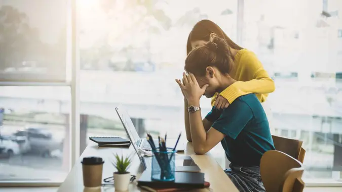 Coworker comforting stressed and discouraged woman in office.