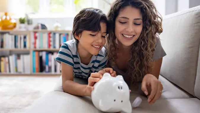 A mother sits next to her son as they open a piggy bank and talk about personal finance and financial literacy. Kids and money concept.