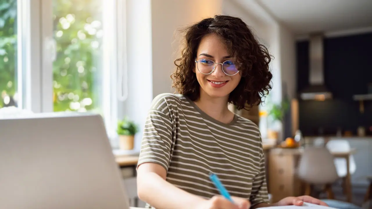 A woman smiles while working from home and looking at her laptop.