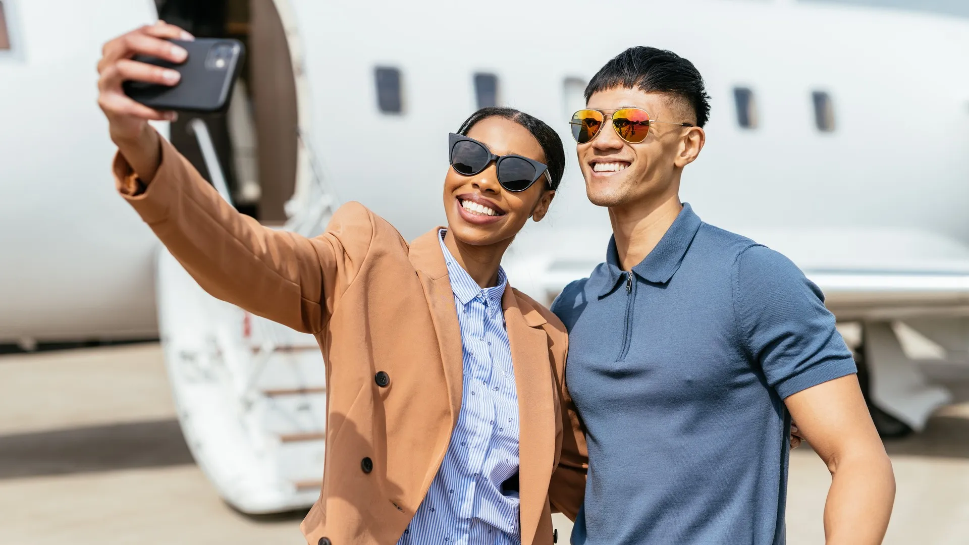 A wealthy couple takes a photo in front of their private jet.