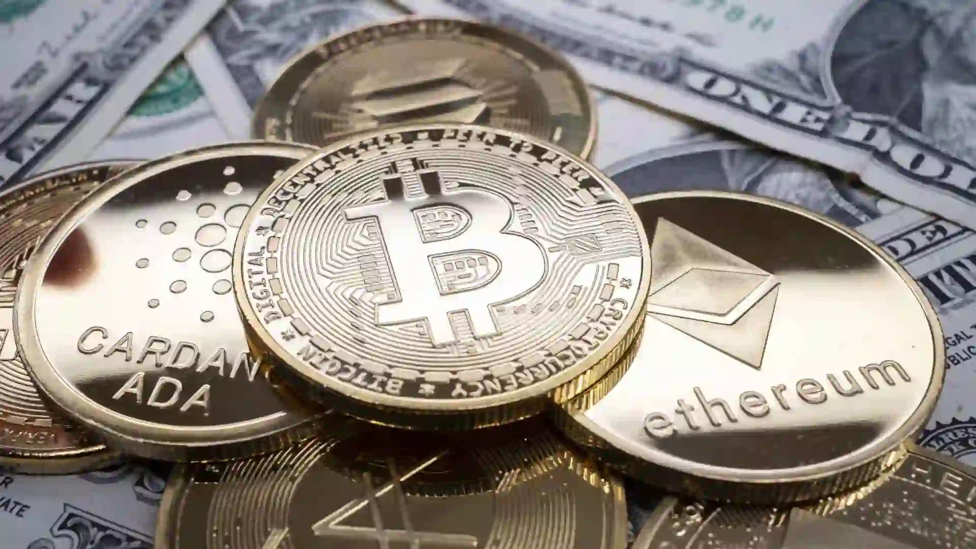 A selection of different cryptocurrency coins piled together over US dollar banknotes.