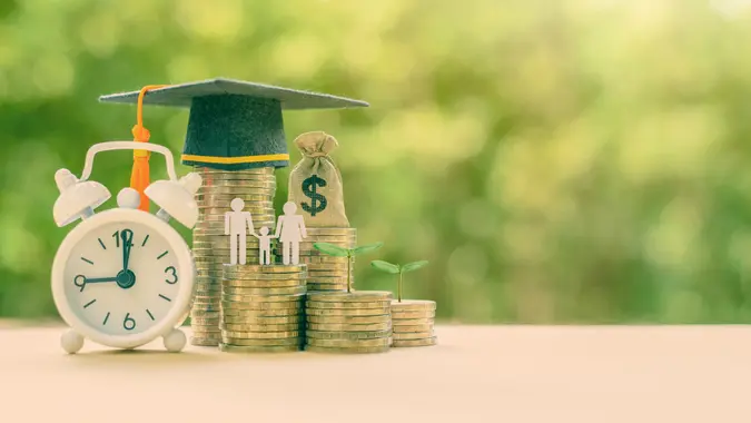 Public school funding / education funding, financial concept : Black graduation cap / hat, family members and kid, US dollar bag on rows of rising coins, white clock on a table, green bokeh background.