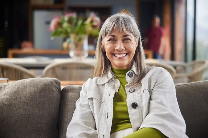 Mature woman smiling while relaxing on a sofa in the living room of her luxury home.