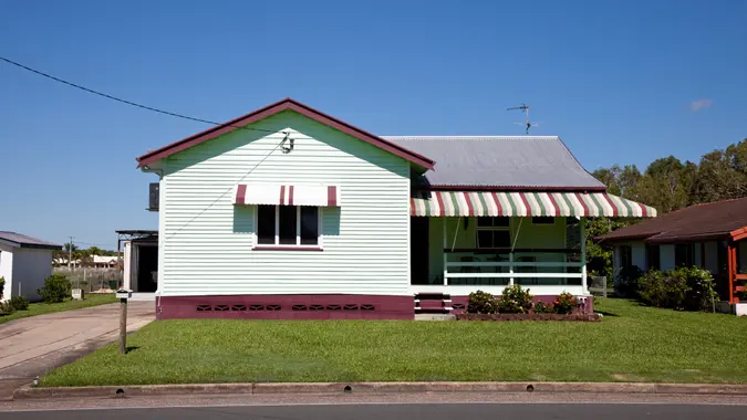 Tidy little old style house with clear blue sky and green grass and overhead power line connected to it – Queensland Australia.