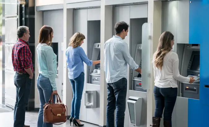 Group of people in a line at an ATM waiting to make a cash withdrawal.