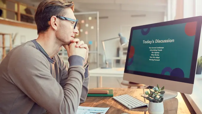 Side view portrait of adult businessman looking at computer screen while preparing for presentation or online conference at desk in office, copy space.