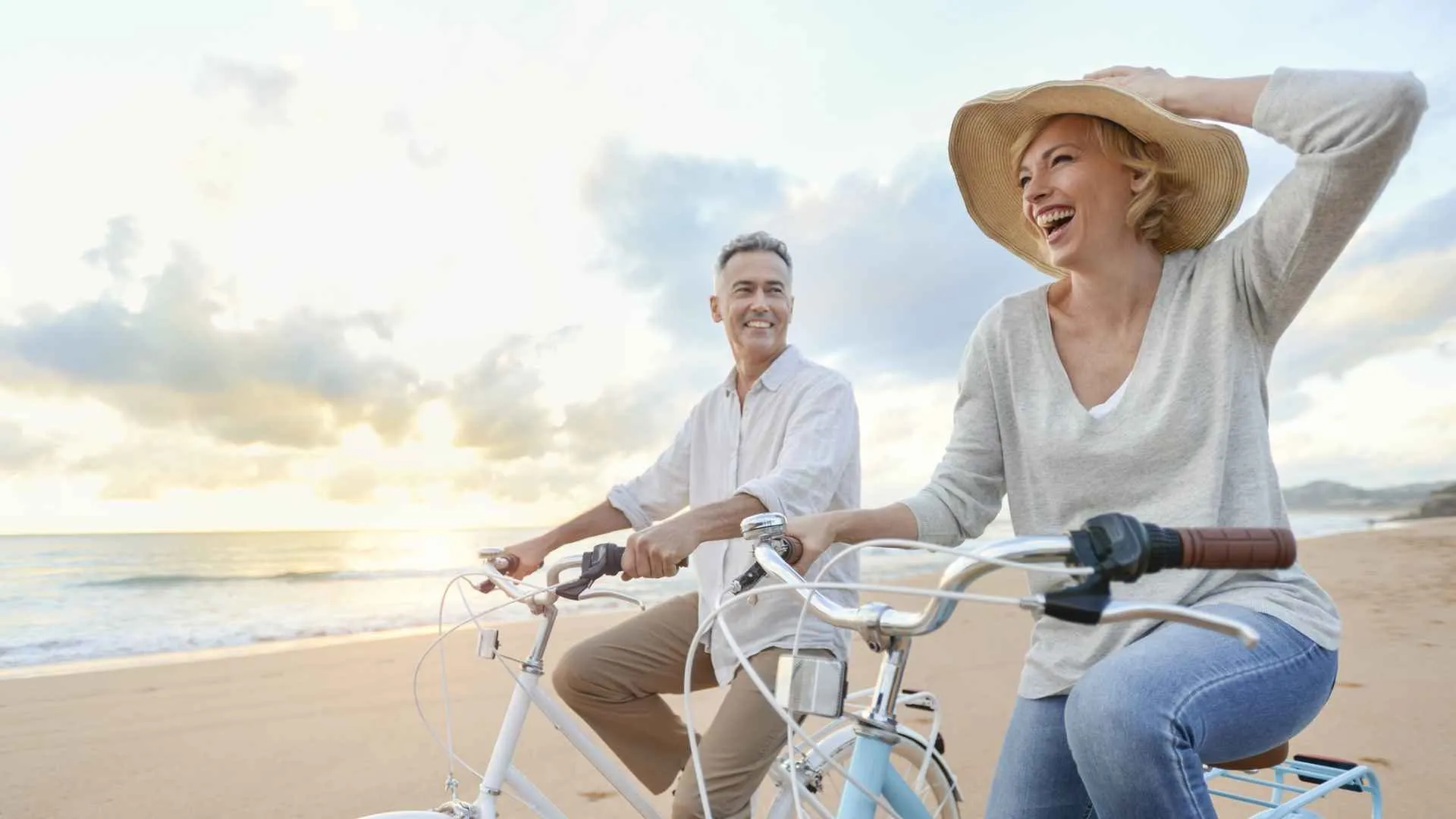 Mature couple cycling on the beach at sunset or sunrise.