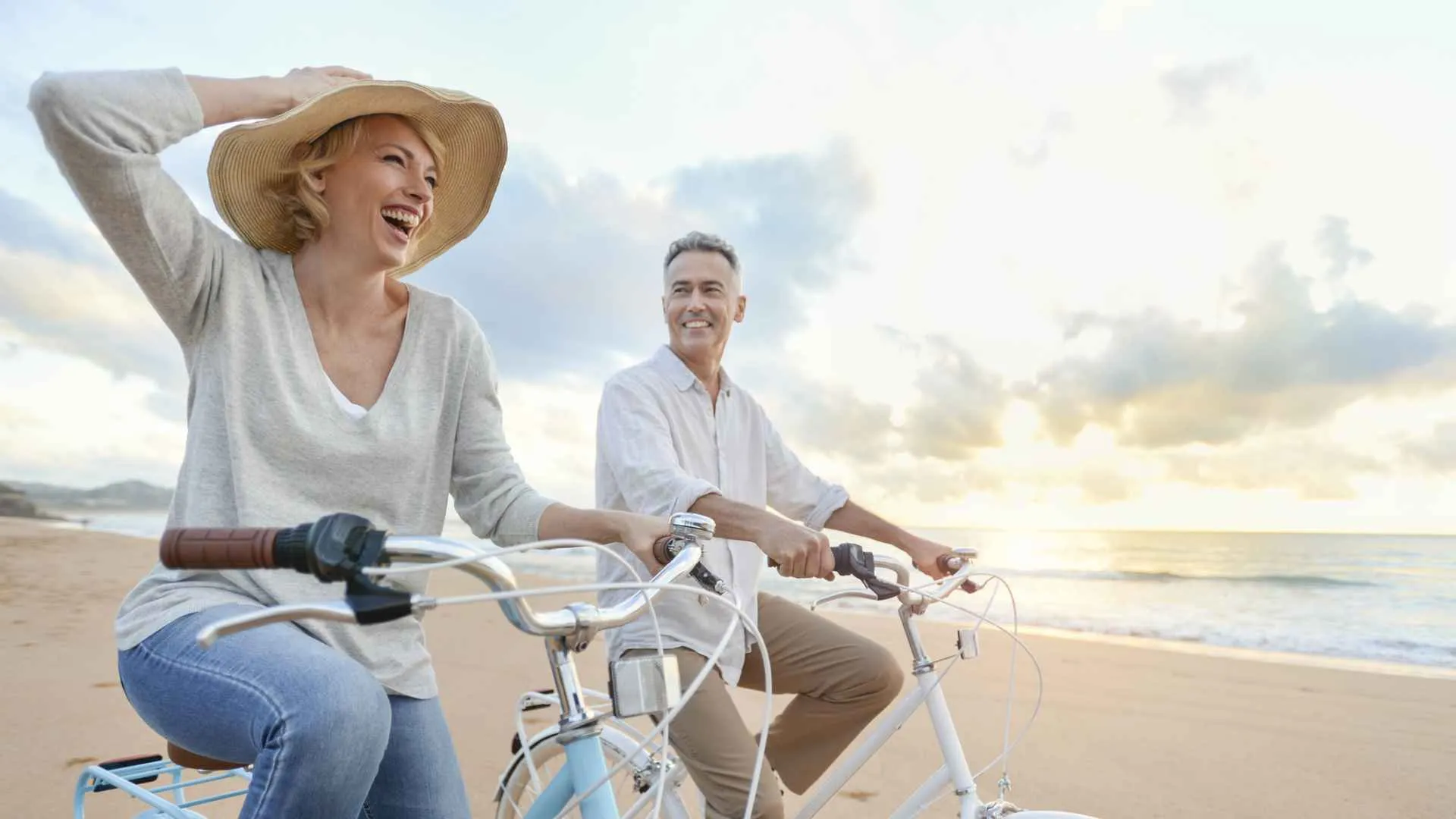 Mature couple cycling on the beach at sunset or sunrise.
