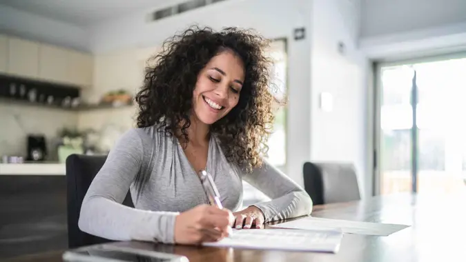 A woman smiles as she files her taxes and works on her budget.